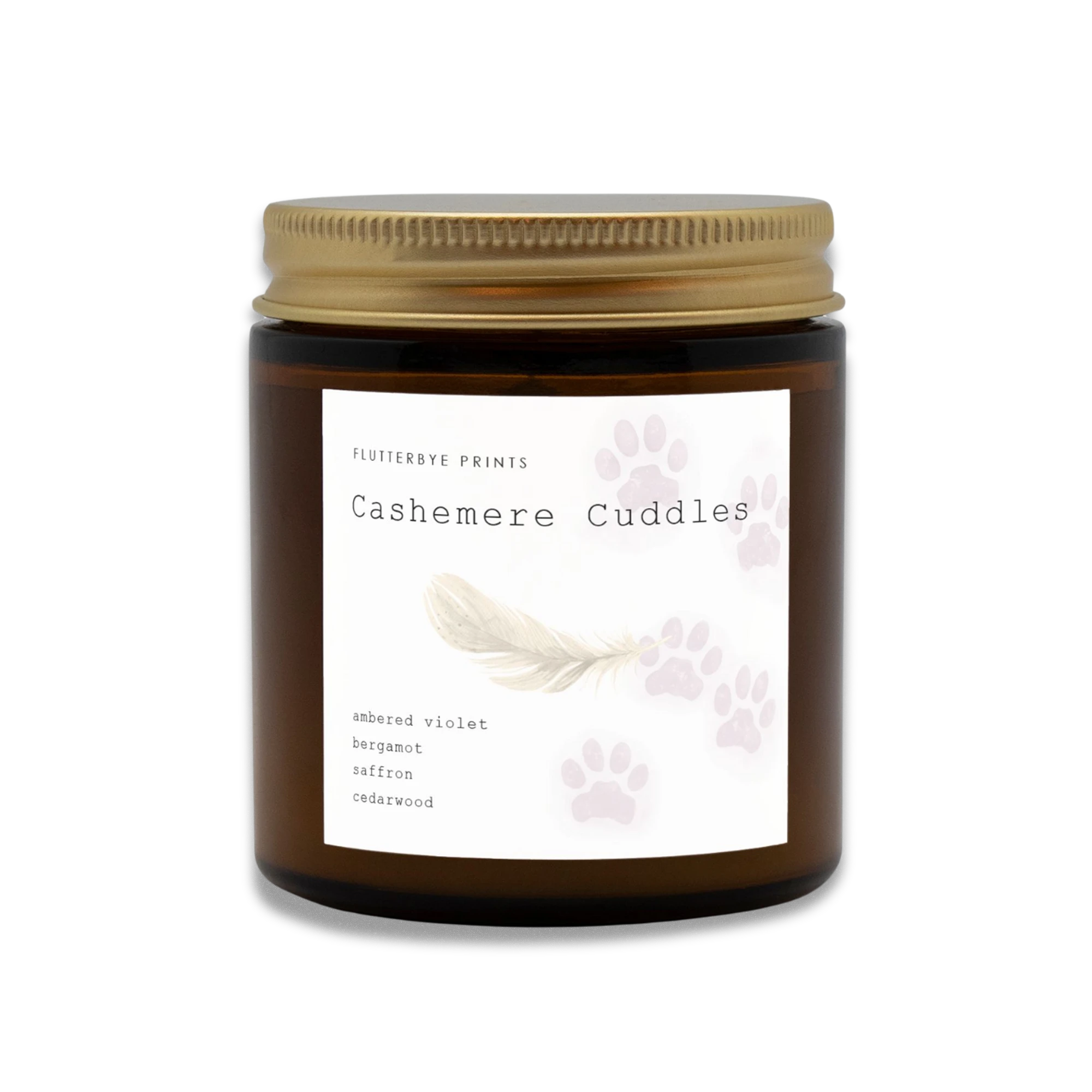 Brown jar candle with a gold lid labeled "Cashemere Cuddles." The label features purple cat paw prints, a feather, and scent notes: violet, bergamot, saffron, cedarwood.