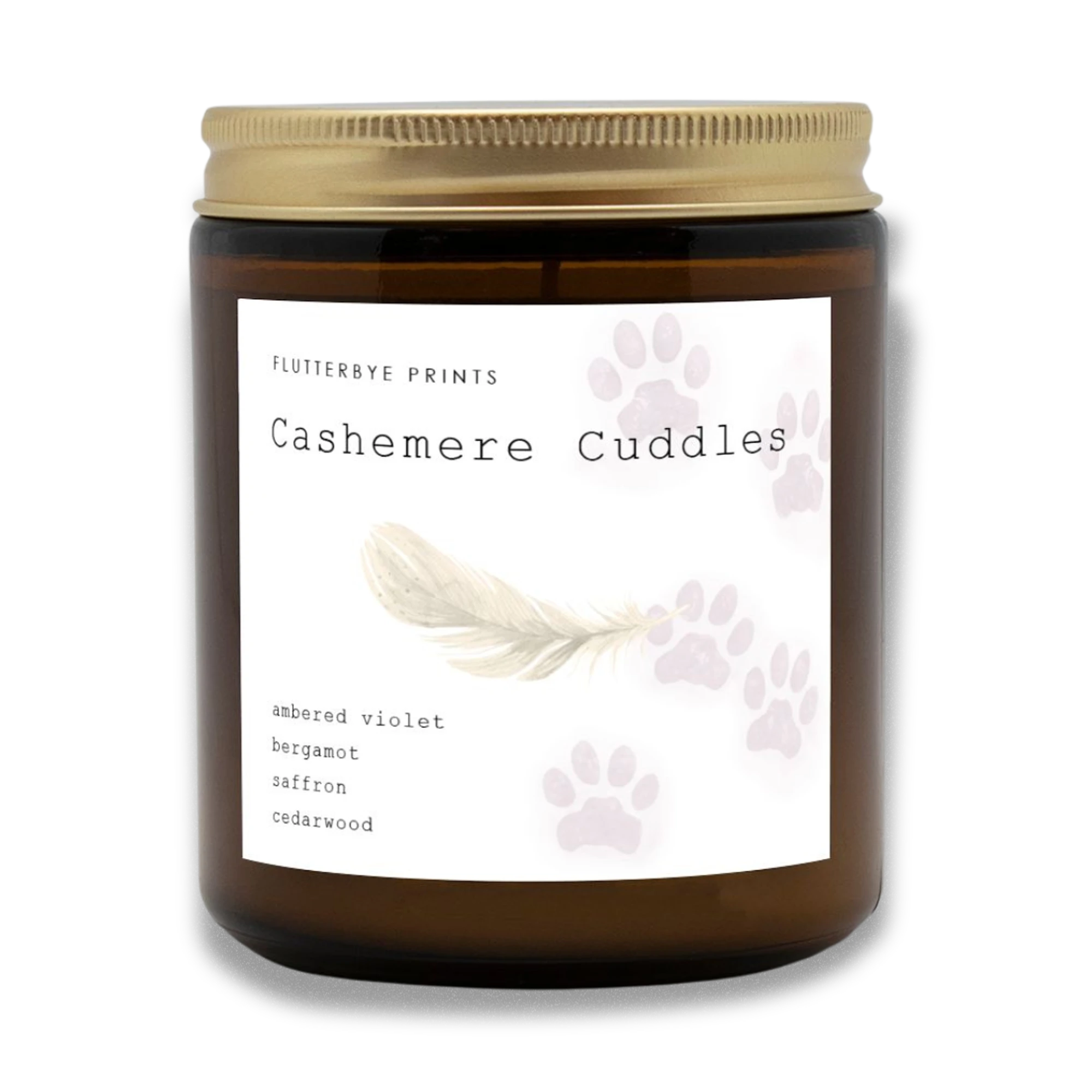 Amber glass candle jar with gold lid labeled "Cashemere Cuddles." Decorated with a feather and watercolor cat paw prints. Fragrances include violet and cedarwood.