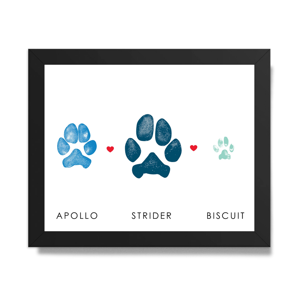 Framed art featuring two dog paw prints and one cat paw print in blue shades with small red hearts between them. Below are the names 