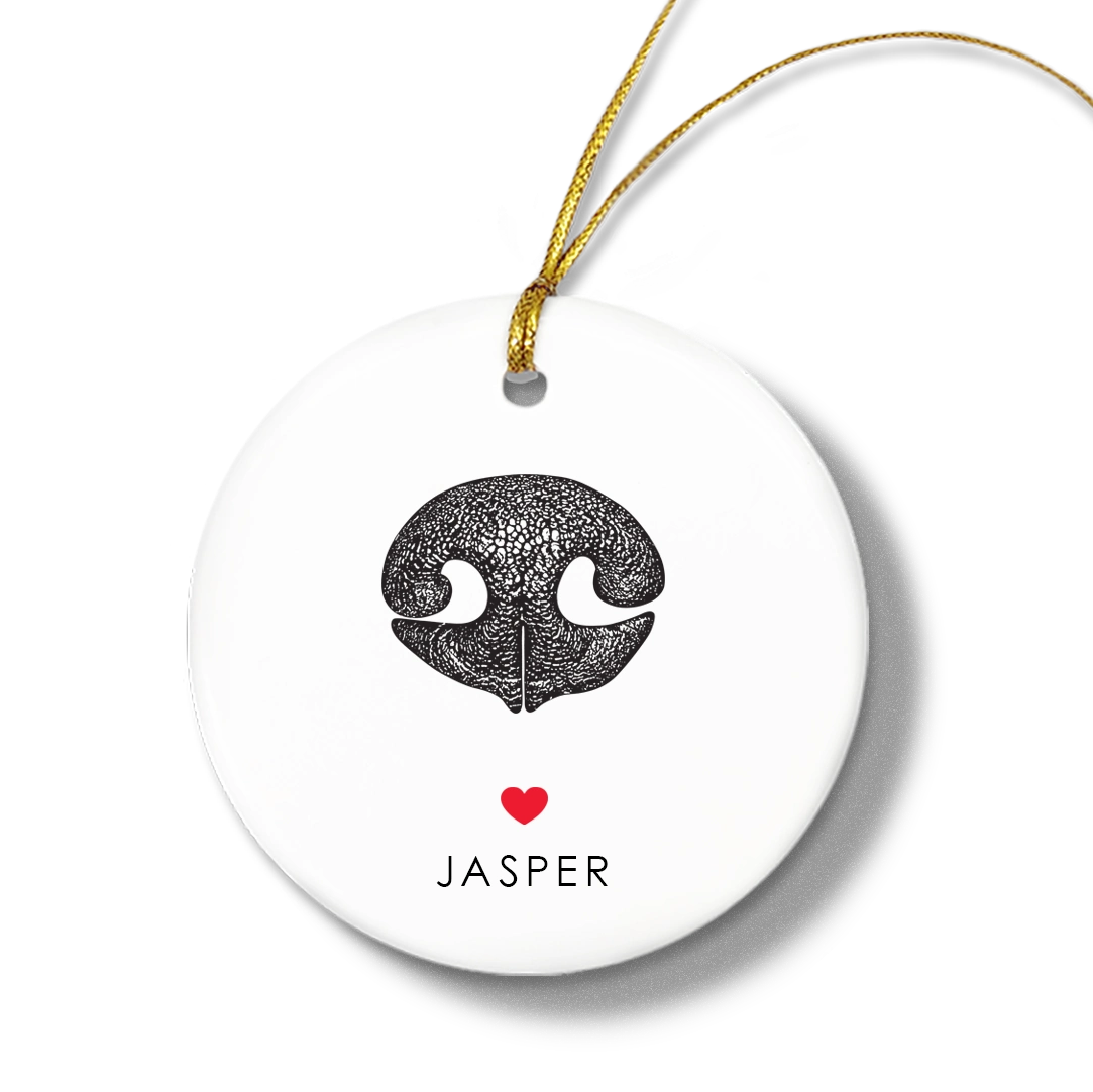 Round white ornament with a textured black dog nose print, small red heart, and the name “Jasper” beneath. Gold string for hanging attached at the top.