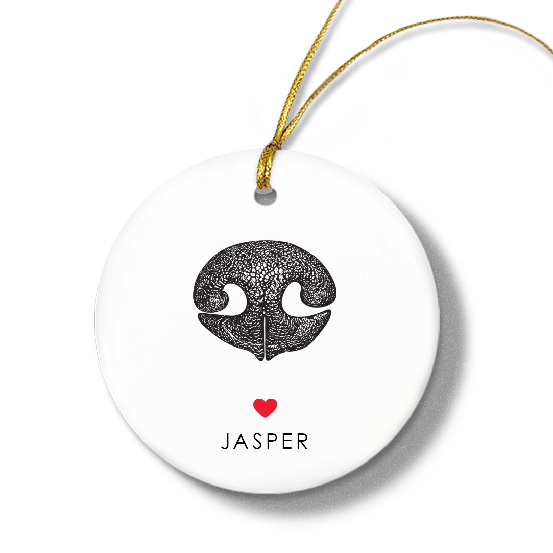 Round white ornament with a textured black dog nose print, small red heart, and the name “Jasper” beneath. Gold string for hanging attached at the top.