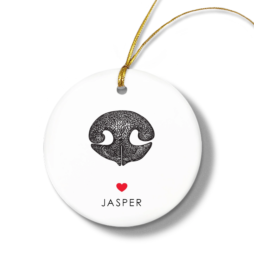 Round white ornament with a textured black dog nose print, small red heart, and the name “Jasper” beneath. Gold string for hanging attached at the top.