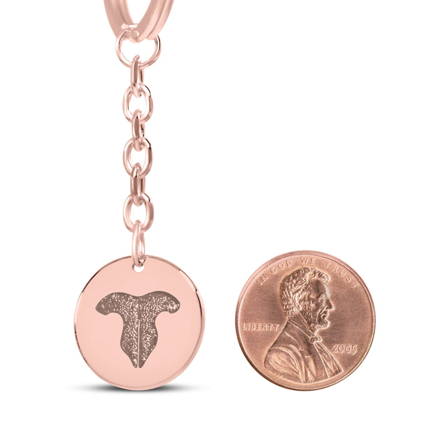 Rose gold coin pendant keychain with featuring an engraved cat paw print design, displayed next to a penny for size comparison.