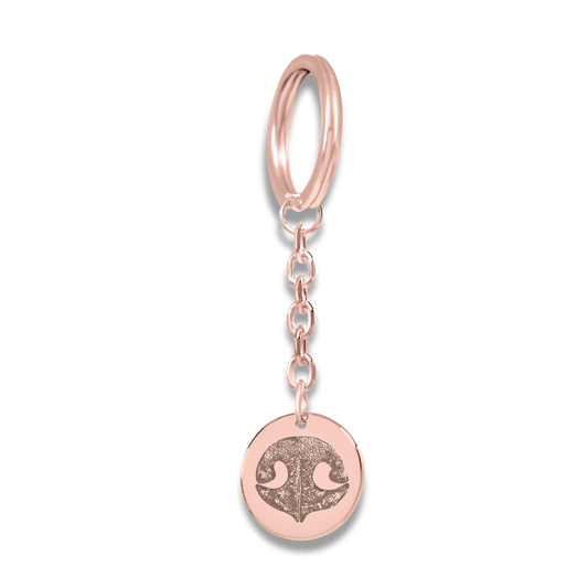 A rose gold keychain with a round pendant featuring a custom dog nose print.