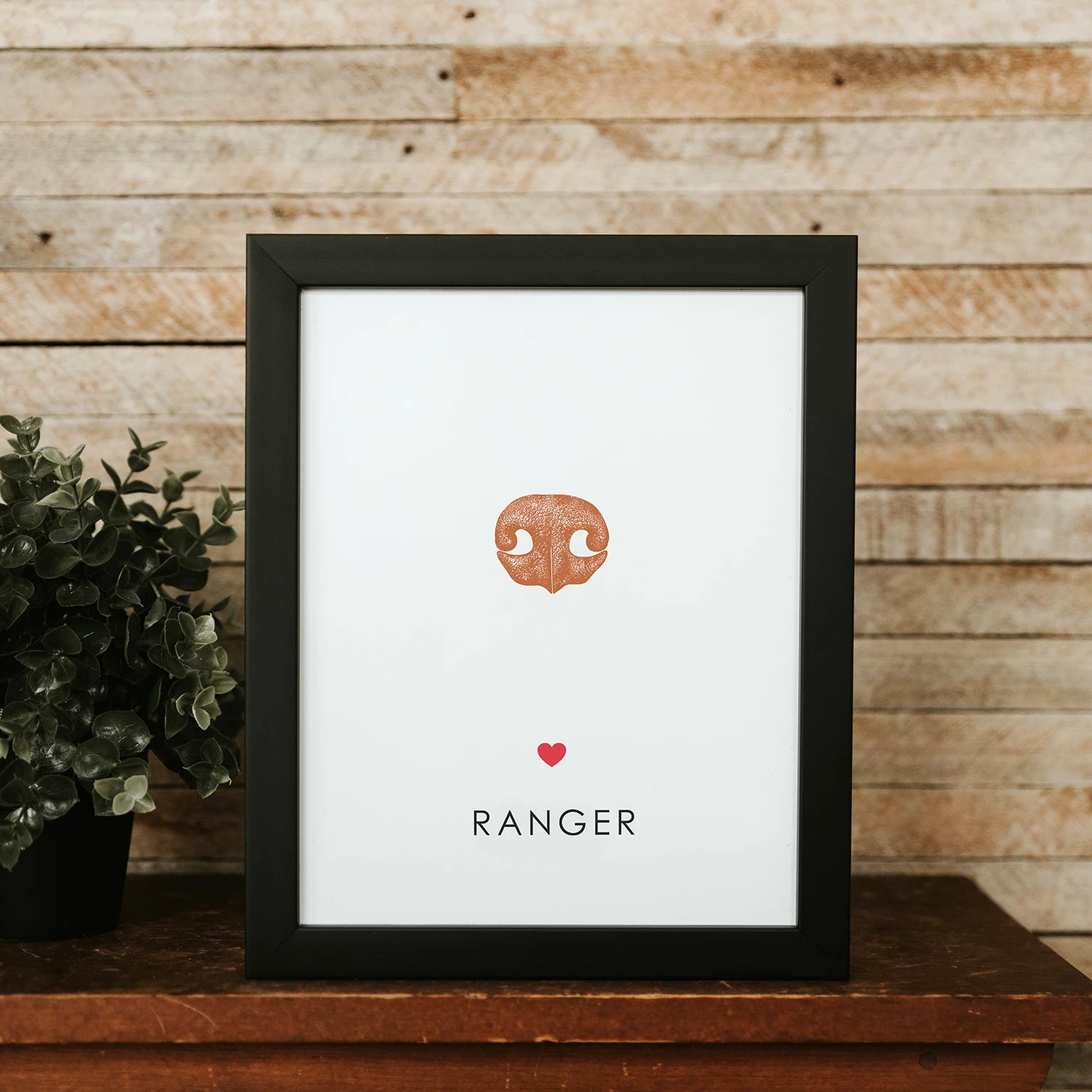 Framed white artwork with a blue dog nose print centered in the middle. Below it is a small red heart and the name "KONA" in bold letters.