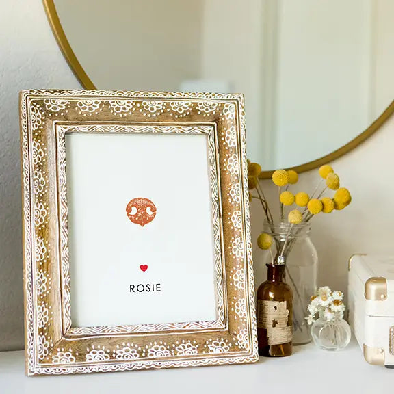 Elegant photo frame with a decorative pattern, placed on a white surface. It features an illustration and the name 