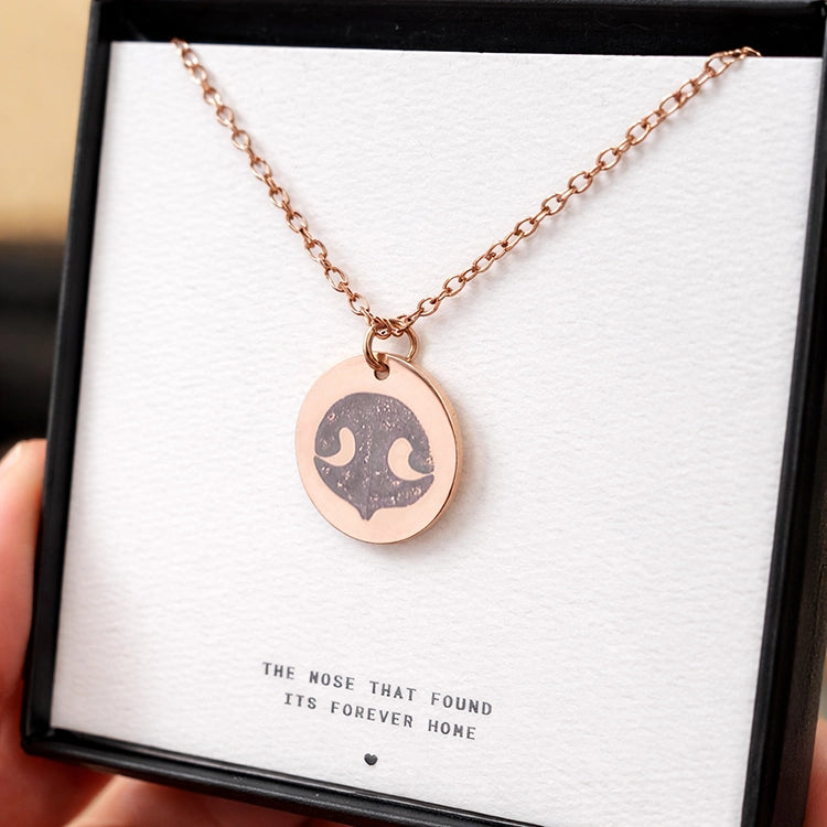 Rose gold necklace with a round pendant featuring a dog's nose print, set against a white background. The text reads, "The nose that found its forever home."
