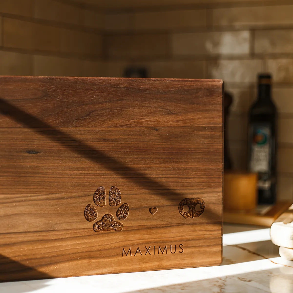 A walnut wood cutting board engraved with a paw print, heart, and dog nose print, with the name 