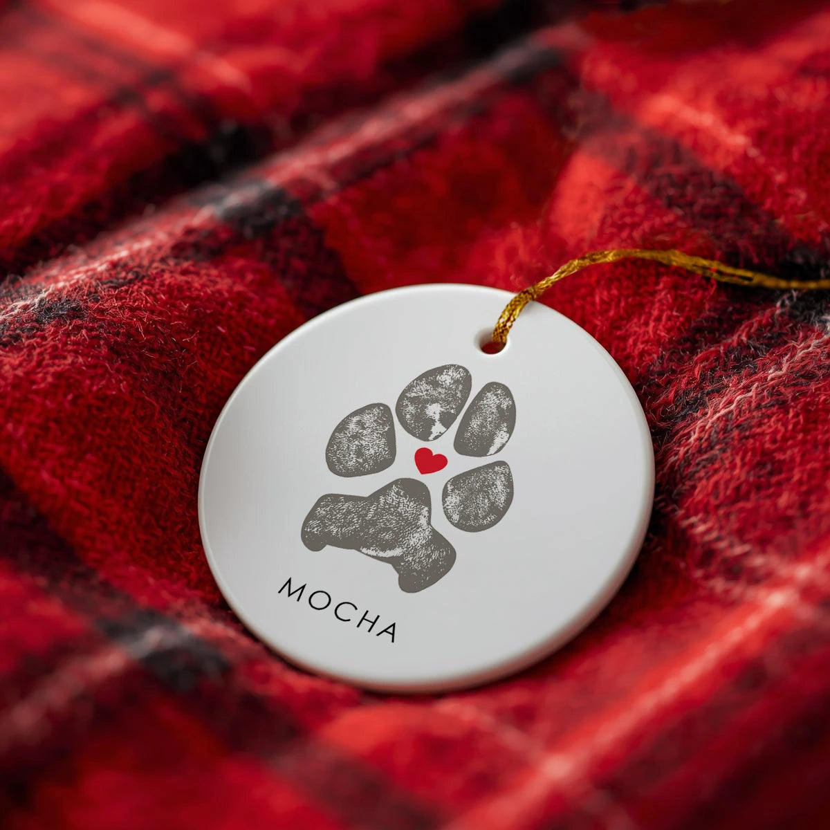 White ceramic ornament with a green cat paw print design, red heart, and "Posie" text. A gold string is attached, to hang on a Christmas tree as a memorial in remembrance of pet.