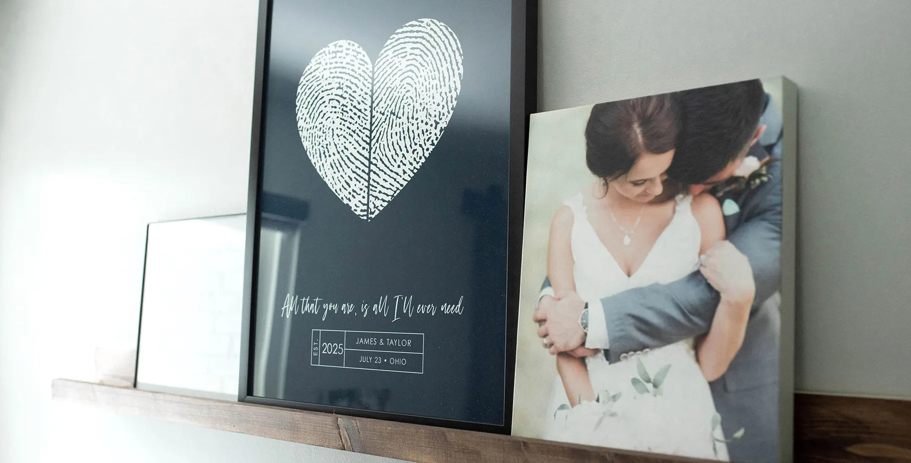 Framed art on a shelf features a heart shape made from fingerprints and text, alongside a photo of a couple in an embrace. The tone is romantic and intimate.