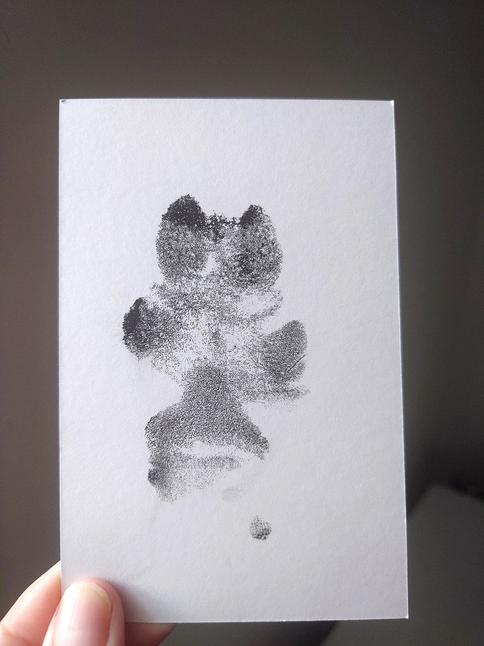 A hand holds a small white card featuring an black dog paw print made form an inkless paw print kit.