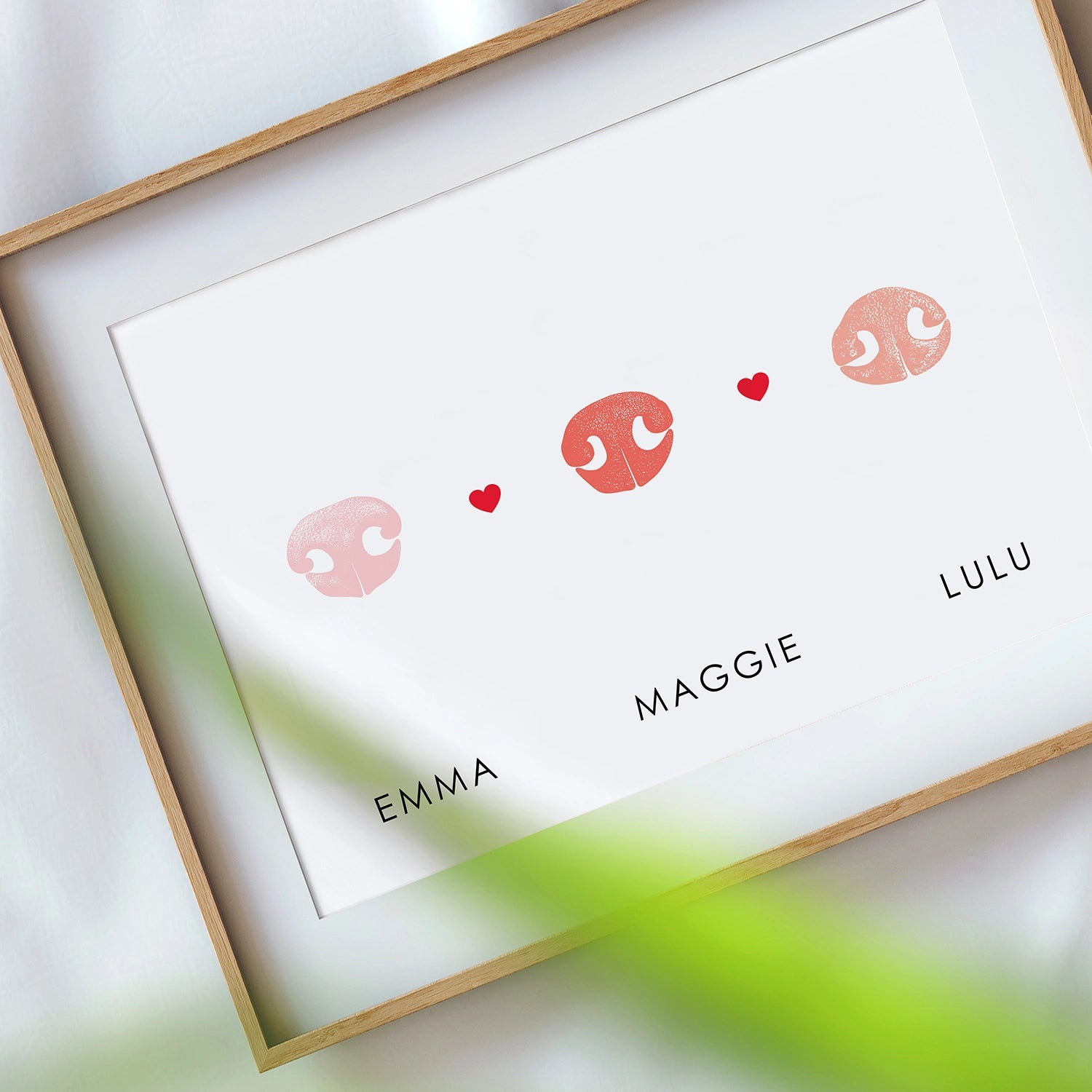 Framed print with three pink dog noses and small red hearts between them. Below, the names Emma, Maggie, and Lulu are printed, conveying a sense of affection.