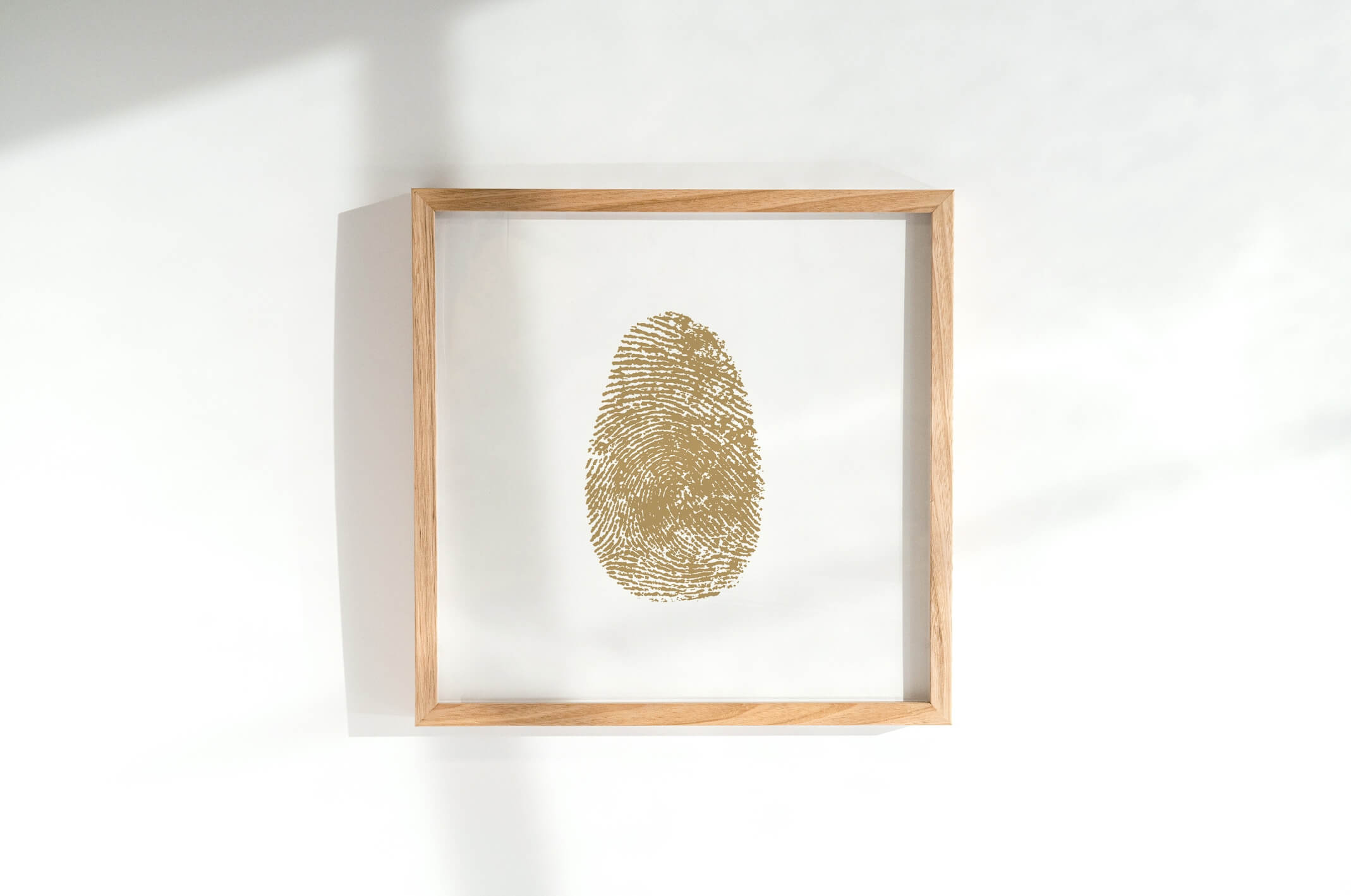 Single large gold fingerprint in wooden frame hanging on white wall.