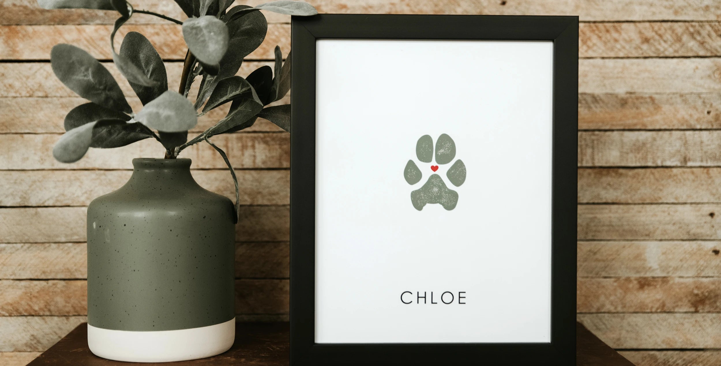 Framed artwork features a sage green dog paw print with a small red heart inside of it, labeled with pet's name 