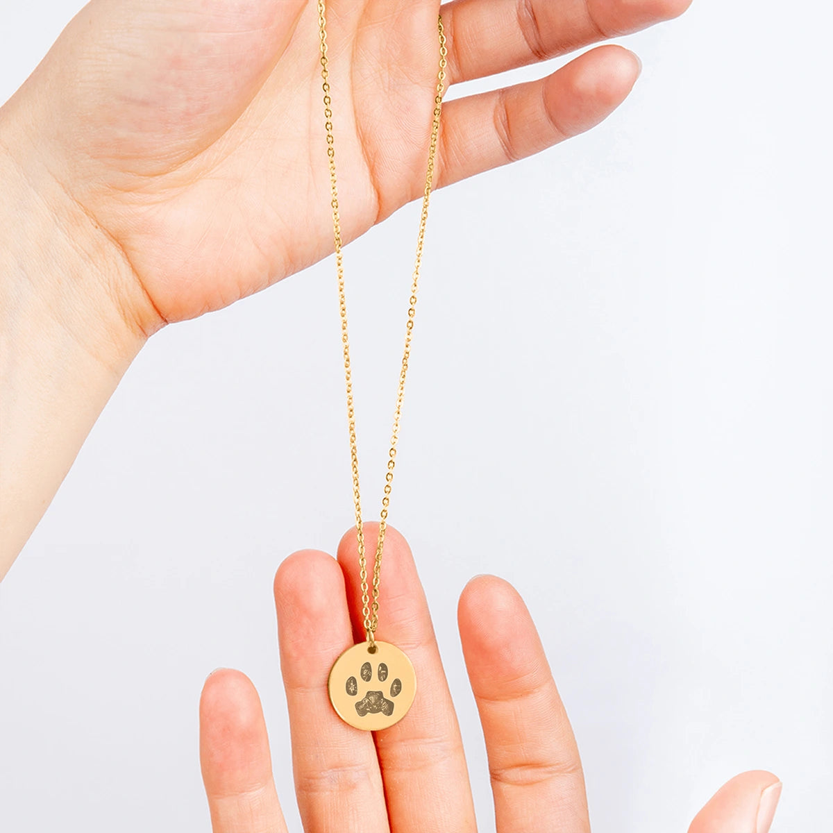 Gold necklace with a round pendant featuring an engraved paws printing. The simple, elegant design conveys warmth and affection, ideal for pet memorial gift.