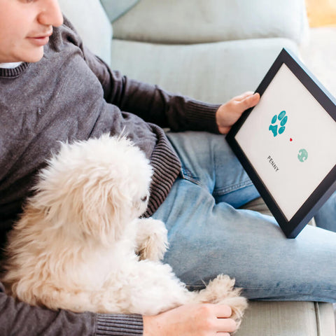 man sitting with pet dog holding framed paw and nose print keepsake art