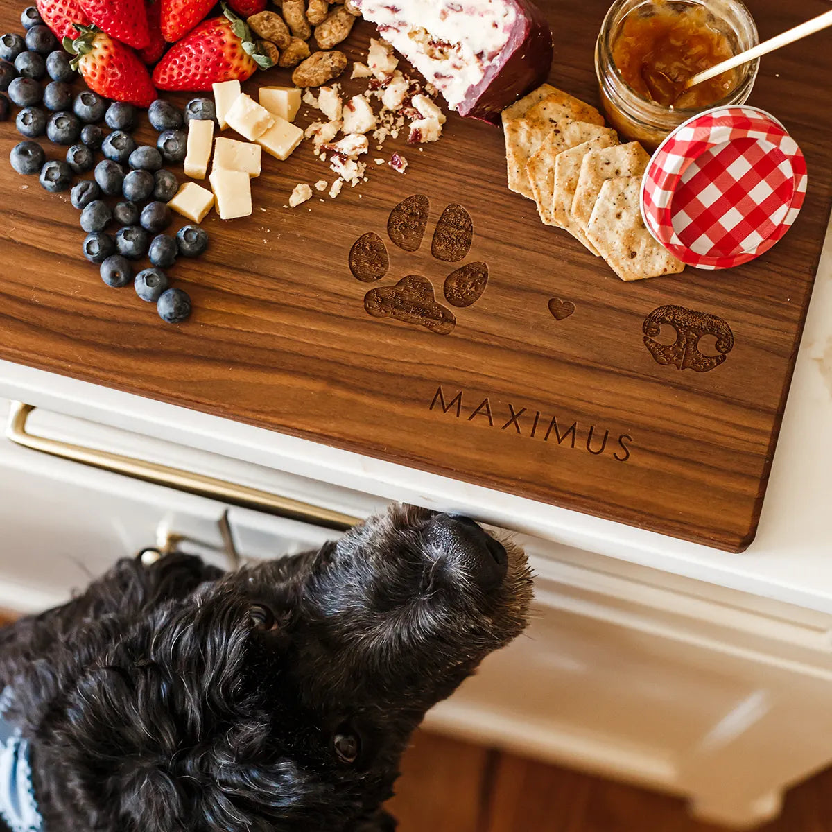 Wooden cutting board with a dark paw print, heart, and nose design engraved above the word 