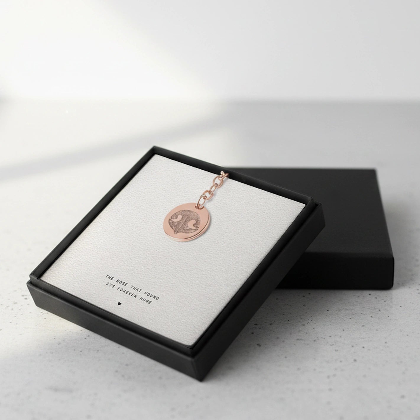 Rose gold keychain with a pendant featuring a dog nose print, set in a gift box with the phrase "The nose that found its forever home".