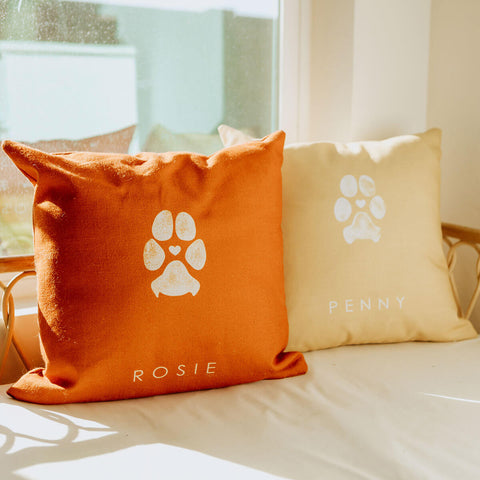 two dog paw print pillows on seat one in orange and the other is cream colored
