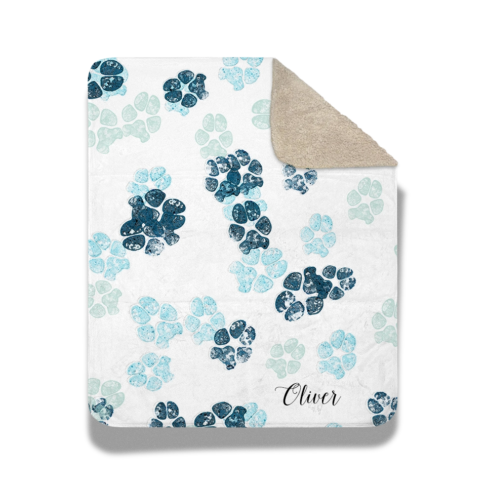 White blanket with scattered custom pet paw prints in shades of blue. The design feels playful.