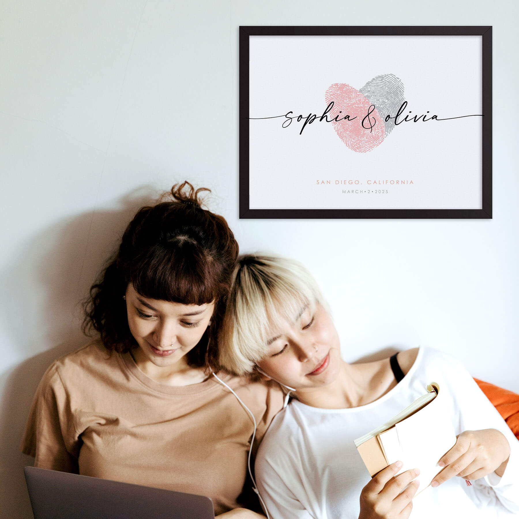 female couple sits together under custom fingerprint heart artwork