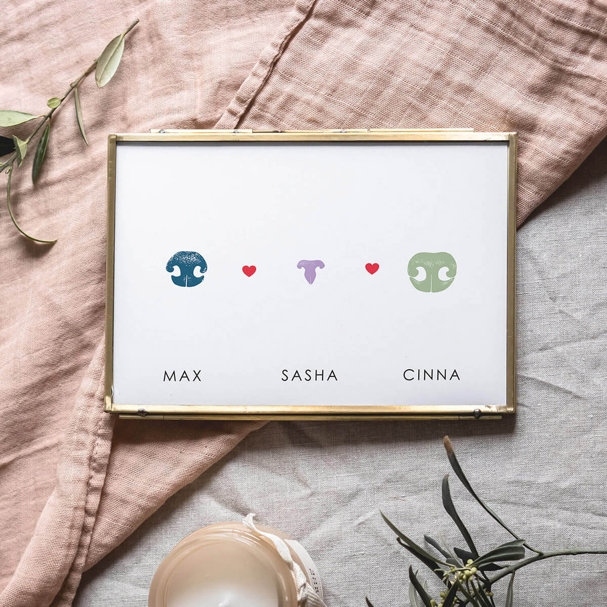 Custom pet loss memorial art with two dog noses and one cat nose laid on soft linen fabric next to candle